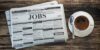 Job classifieds ads newspaper and coffee cup on wooden table. Job search concept.